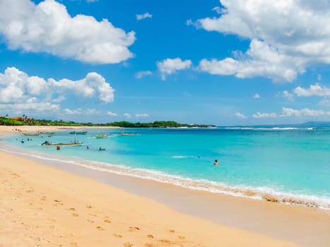 Beautiful white sand beach surrounded by tropical palm trees on the island of Bali in Nusa Dua area. Blue sky with white clouds, white sand and palm trees.