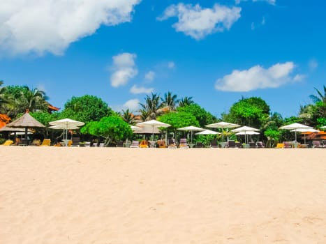 Beautiful white sand beach surrounded by tropical palm trees on the island of Bali in Nusa Dua area. Blue sky with white clouds, white sand and palm trees.