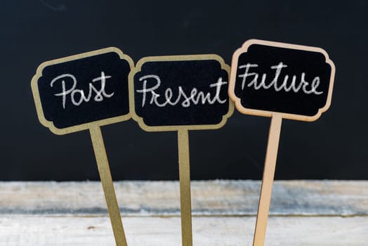 Business message Past, Present, Future written with chalk on wooden mini blackboard labels, defocused chalkboard and wood table in background