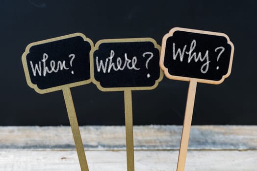 Business message When ? Where ? Why ? written with chalk on wooden mini blackboard labels, defocused chalkboard and wood table in background