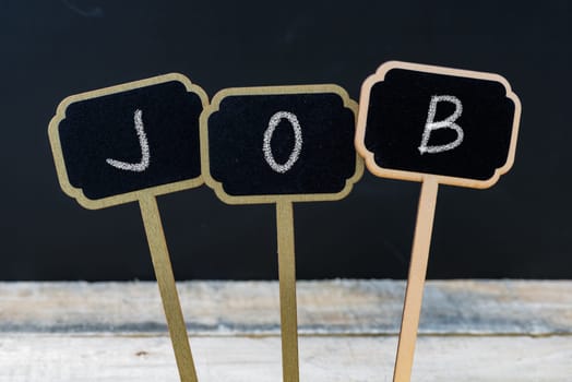 Business message JOB written with chalk on wooden mini blackboard labels, defocused chalkboard and wood table in background