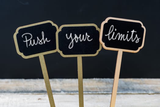 Motivational message Push Your Limits written with chalk on wooden mini blackboard labels, defocused chalkboard and wood table in background