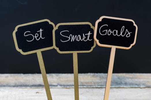 Business message Set Smart Goals written with chalk on wooden mini blackboard labels, defocused chalkboard and wood table in background