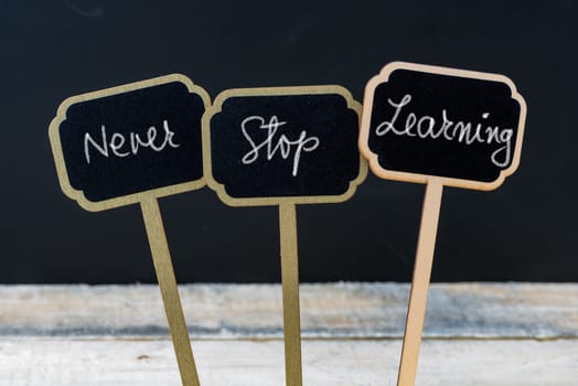 Motivational message Never Stop Learning written with chalk on wooden mini blackboard labels, defocused chalkboard and wood table in background