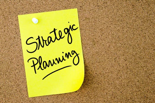 Strategic Planning text written on yellow paper note pinned on cork board with white thumbtack. Business concept image with copy space available