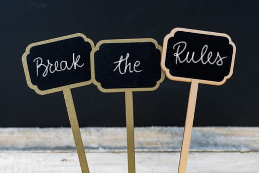 Motivational message Break The Rules written with chalk on wooden mini blackboard labels, defocused chalkboard and wood table in background