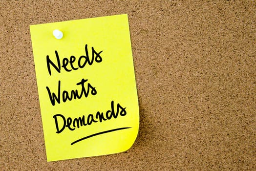 Needs, Wants, Demands text written on yellow paper note pinned on cork board with white thumbtack. Business concept image with copy space available