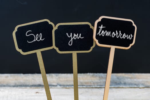 Business message See You Tomorrow written with chalk on wooden mini blackboard labels, defocused chalkboard and wood table in background