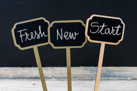 Business message Fresh New Start written with chalk on wooden mini blackboard labels, defocused chalkboard and wood table in background