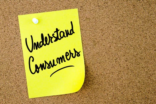 Understand Consumers text written on yellow paper note pinned on cork board with white thumbtack. Business concept image with copy space available