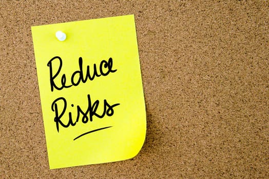 Reduce Risks text written on yellow paper note pinned on cork board with white thumbtack. Business concept image with copy space available