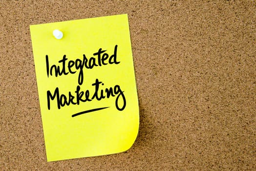 Integrated Marketing text written on yellow paper note pinned on cork board with white thumbtack. Business concept image with copy space available