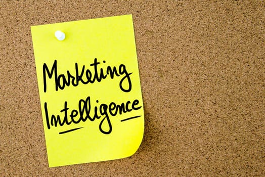 Marketing Intelligence text written on yellow paper note pinned on cork board with white thumbtack. Business concept image with copy space available