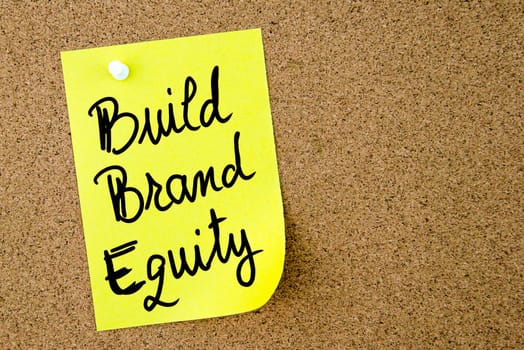 Build Brand Equity text written on yellow paper note pinned on cork board with white thumbtack. Business concept image with copy space available