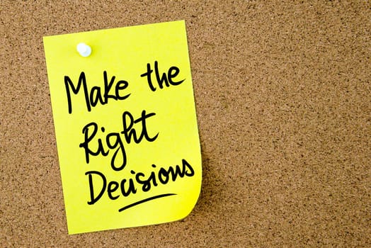 Make The Right Decisions text written on yellow paper note pinned on cork board with white thumbtack. Business concept image with copy space available