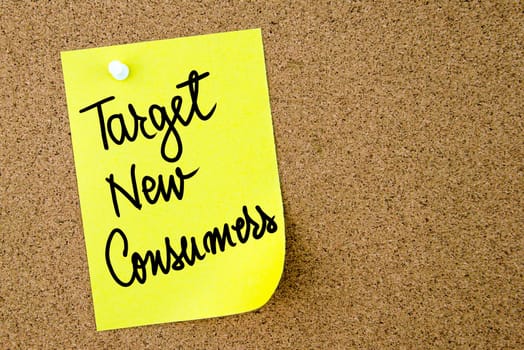 Target New Consumers text written on yellow paper note pinned on cork board with white thumbtack. Business concept image with copy space available