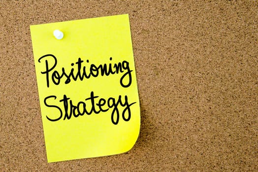 Positioning Strategy text written on yellow paper note pinned on cork board with white thumbtack. Business concept image with copy space available