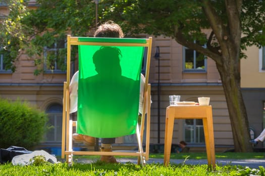 Silhouette of relaxed man chilling on deckchair in urban city park