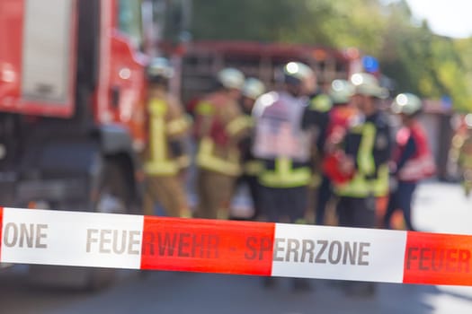 Team of blured firefighters by firetruck on protected accident site. Focus on red and white security band.