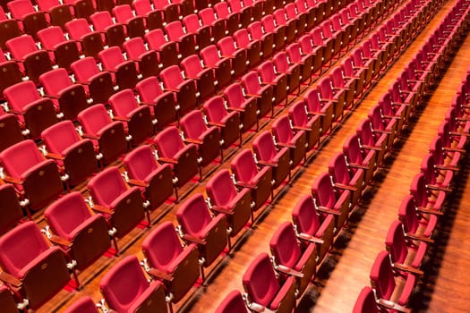Rows of red color theatre chairs in conference room.