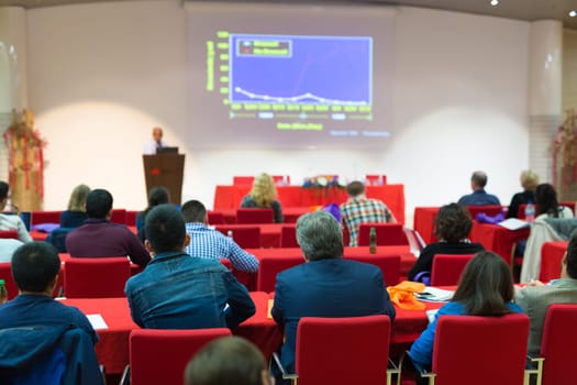 Speaker Giving a Talk at Business Meeting. Audience in the conference hall. Business and Entrepreneurship. Focus on unrecognizable people from rear.