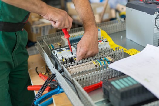 Electrician assembling industrial electric cabinet in workshop.
