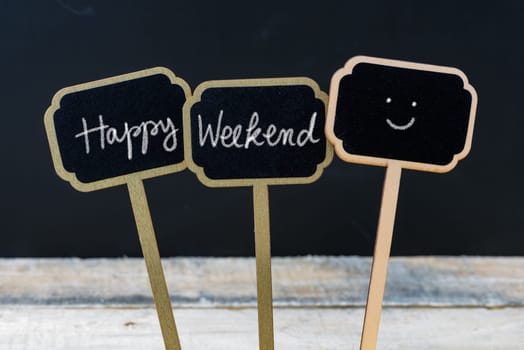 Motivational message Happy Weekend written with chalk on wooden mini blackboard labels, defocused chalkboard and wood table in background
