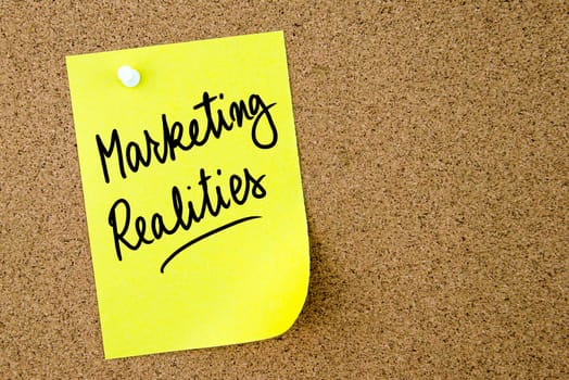 Marketing Realities text written on yellow paper note pinned on cork board with white thumbtack. Business concept image with copy space available