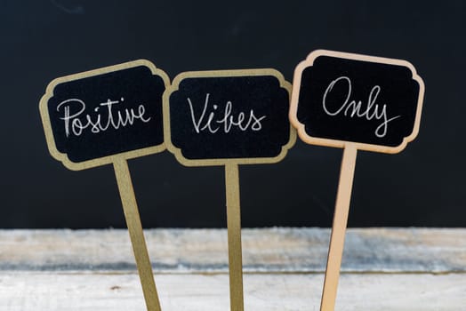 Motivational message Positive Vibes Only written with chalk on wooden mini blackboard labels, defocused chalkboard and wood table in background