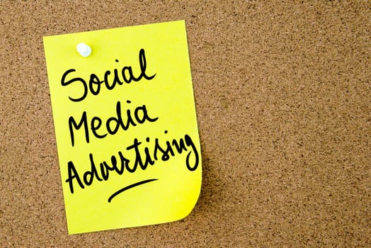 Social Media Advertising text written on yellow paper note pinned on cork board with white thumbtack. Business concept image with copy space available