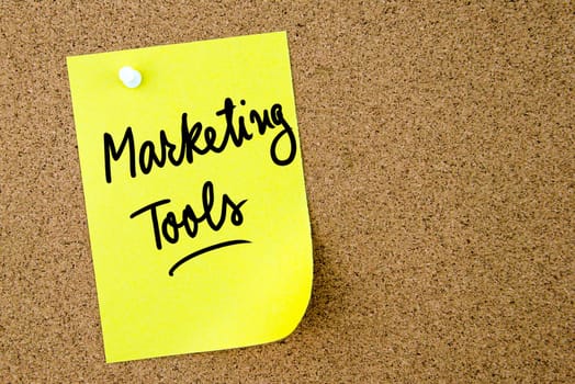 Marketing Tools text written on yellow paper note pinned on cork board with white thumbtack. Business concept image with copy space available