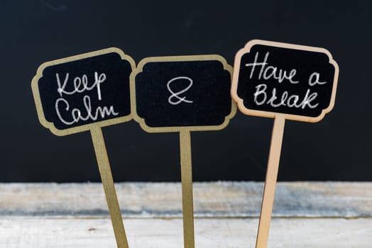 Motivational message Keep Calm and Have a Break written with chalk on wooden mini blackboard labels, defocused chalkboard and wood table in background
