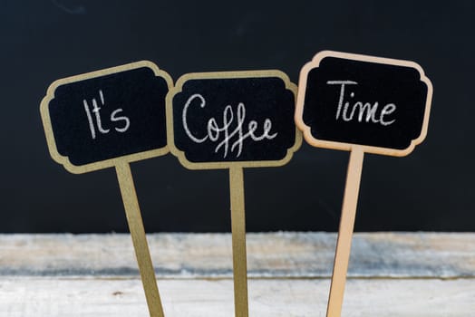 Motivational message Its Coffee Time written with chalk on wooden mini blackboard labels, defocused chalkboard and wood table in background