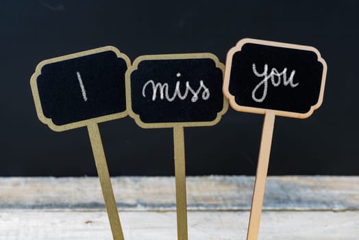 Motivational message I MISS YOU written with chalk on wooden mini blackboard labels, defocused chalkboard and wood table in background