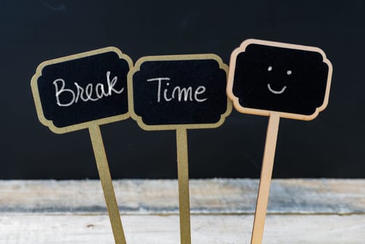 Motivational message Break Time written with chalk on wooden mini blackboard labels, defocused chalkboard and wood table in background