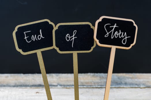 Motivational message End Of Story written with chalk on wooden mini blackboard labels, defocused chalkboard and wood table in background