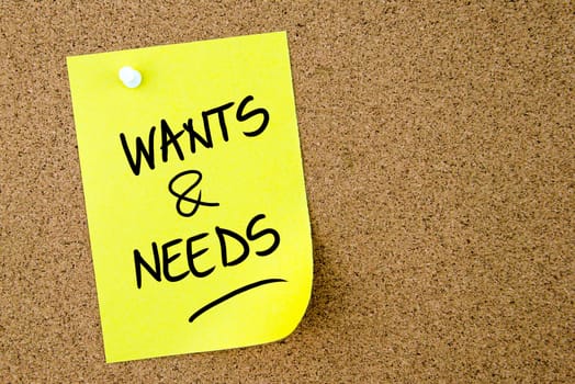 Wants and Needs text written on yellow paper note pinned on cork board with white thumbtack. Business concept image with copy space available