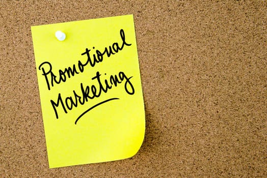 Promotional Marketing text written on yellow paper note pinned on cork board with white thumbtack. Business concept image with copy space available