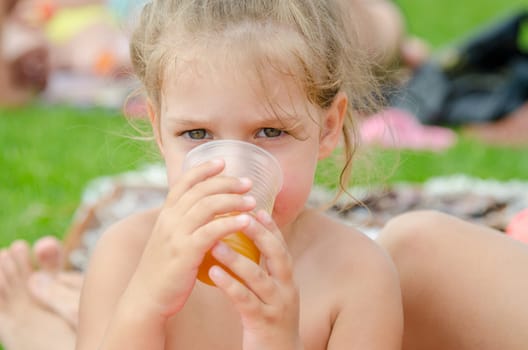 The girl drinks juice from a plastic disposable cup on a picnic