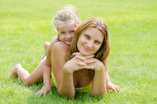 Mum and daughter lie on a green lawn in a bikini and look in the frame