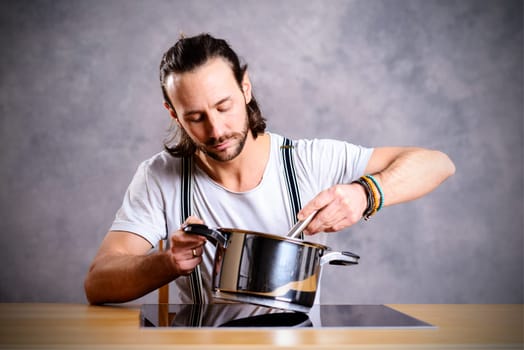 young bearded man with cooking pot and egg whish in front of gray background