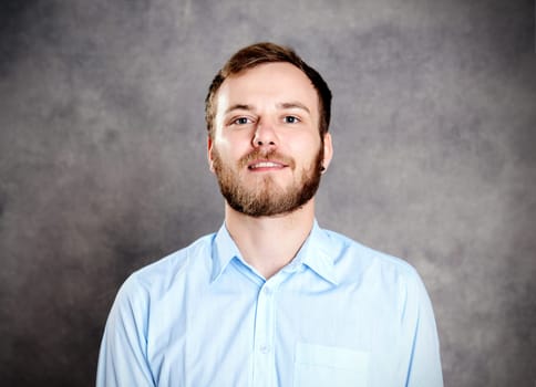 young bearded man in blue shirt in front of gray background
