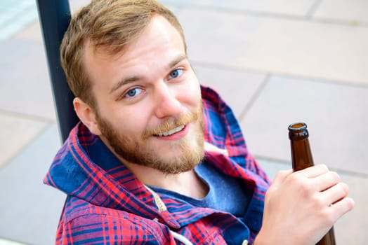 young bearded man with bottle in checkered shirt sitting on stairs