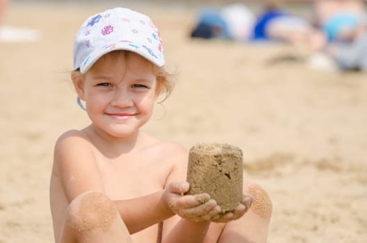 Girl keeps hands on the turret of sand sitting on a river beach
