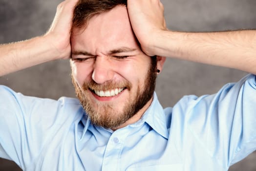 young bearded man in front of gray background has headache