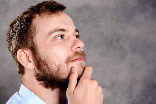 young bearded man in front of gray background is reflecting