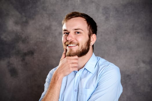young bearded man in front of gray background is reflecting