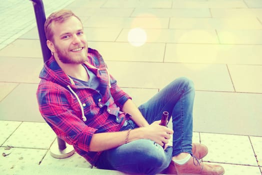 young bearded man with bottle in checkered shirt sitting on stairs