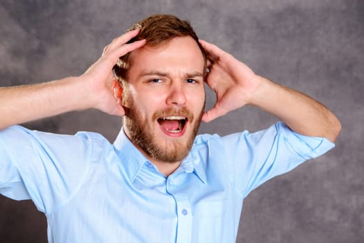 young bearded man in front of gray background has headache