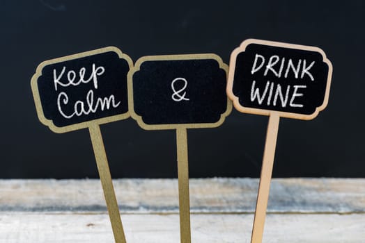 Keep Calm and Drink Wine message written with chalk on mini blackboard labels, defocused chalkboard and wooden table in background. Fun and humor concept